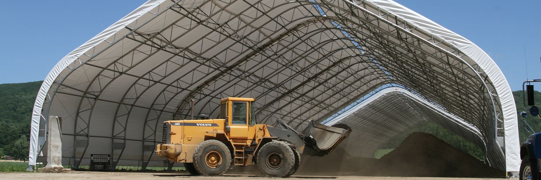 Yellow front loader inside a large industrial tent.