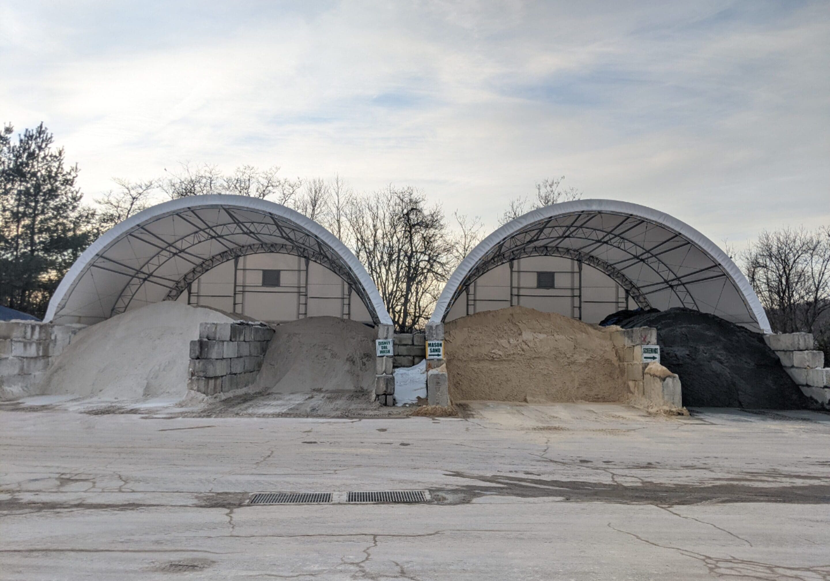 Two large storage tents filled with different bulk materials under a cloudy sky.