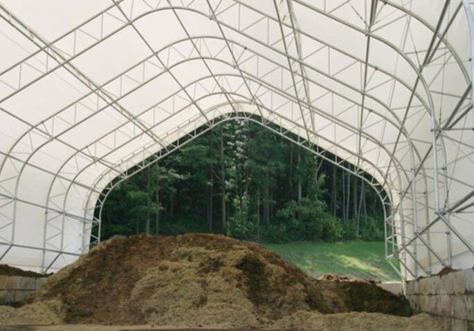 Large indoor soil storage under a translucent roof with a forest backdrop.