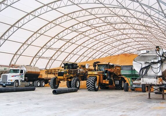 Heavy machinery parked inside a large industrial shelter with a curved roof.